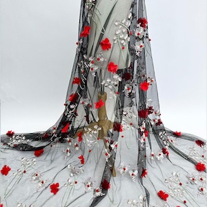 May include: Black sheer fabric with embroidered red and white floral accents. The delicate design features three-dimensional red flowers and silver-toned beaded details, creating a textured and elegant look. Ideal for bridal or formal wear.