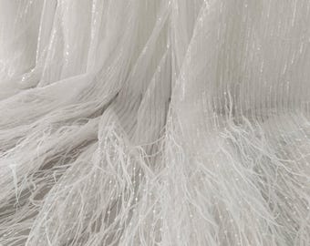 May include: Close-up of white fabric with a delicate, textured appearance. The material features vertical lines and strands, creating a layered effect. The fabric has a soft, flowing drape, with a subtle sheen.
