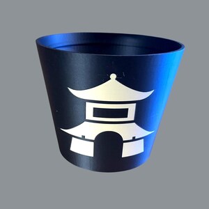 Pode incluir: Um recipiente cónico azul marinho com um design de pagoda branco estilizado. O recipiente tem um acabamento brilhante e uma borda ligeiramente alargada. O design da pagoda está centrado na lateral do recipiente.