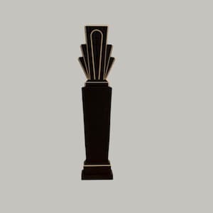 May include: A black art deco style pillar with gold accents. The pillar has a rectangular base and a fan-shaped top. The design is symmetrical and stands against a neutral background. The overall aesthetic is elegant and vintage.