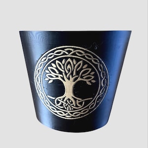 May include: Black cylindrical container with a beige Tree of Life design. The tree is within a circular Celtic knot border. The container has a slightly tapered shape and is set against a light gray background.
