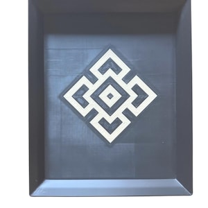 May include: A rectangular, dark gray tray with a geometric design in the center. The design is a white and beige square pattern. The tray has a raised edge.