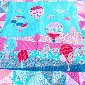 May include: A patchwork quilt with a vibrant design. The quilt showcases a sky blue central panel with appliqued hot air balloons and clouds. The lower section features floral and geometric patterns in pink, teal, and white. The quilt is a mix of textures and patterns.