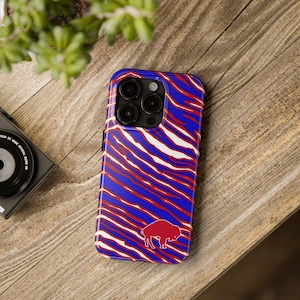 May include: A blue and red patterned phone case featuring a red buffalo logo. The case has a zebra stripe design in red and white over a blue background. The phone case is on a wooden surface.