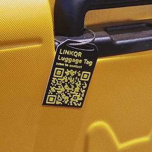 Könnte beinhalten: Ein schwarzes Gepäckanhänger mit dem Text "LINKQR Luggage Tag" und "scan to contact" in Weiß. Das Etikett hat einen gelben QR-Code. Das Etikett ist an einem gelben Koffer befestigt.