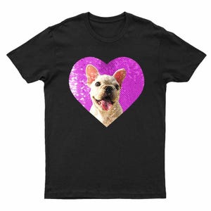 Puede incluir: Camiseta negra con un bulldog franc&eacute;s sonriendo dentro de un coraz&oacute;n rosa. El perro tiene un pelaje de color claro y su lengua es visible. El coraz&oacute;n tiene un aspecto texturizado y brillante. Prenda de vestir informal con tem&aacute;tica de mascotas.