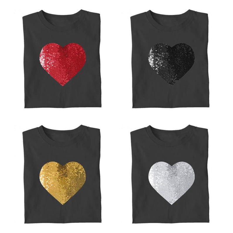 Puede incluir: Cuatro camisetas grises oscuras, cada una con un dise&ntilde;o de coraz&oacute;n con lentejuelas. Los corazones son rojos, negros, dorados y plateados. Las camisetas son sin mangas y tienen cuello redondo.
