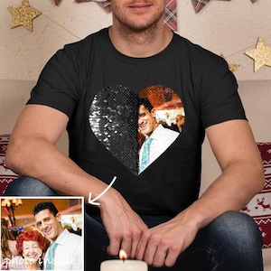 以下が含まれることがあります： 黒いTシャツ、ハートのデザイン。ハートの半分は銀色のスパンコールで覆われ、もう半分は男性の写真を表示しています。男性と女性の小さな写真が左下にあります。「photo inside」の文字が見えます。