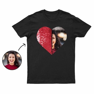 Puede incluir: Camiseta negra con un dise&ntilde;o de coraz&oacute;n. Una mitad del coraz&oacute;n es de lentejuelas rojas, y la otra mitad es una fotograf&iacute;a de una persona. Una peque&ntilde;a foto de la persona est&aacute; en la esquina inferior izquierda. La camiseta tiene cuello redondo.