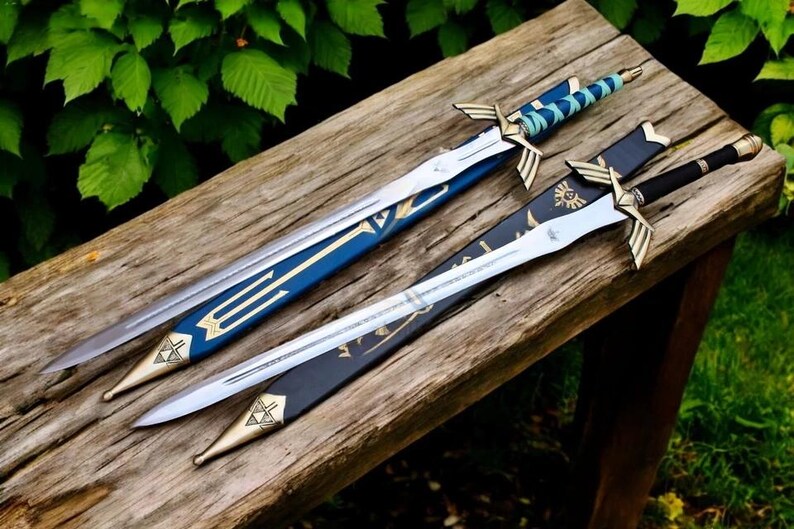 May include: Two decorative swords with silver blades and gold detailing are displayed on a wooden surface. One sword has a blue and gold handle and sheath, the other a black sheath and handle. The swords are displayed outdoors.