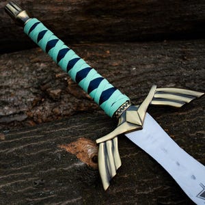 May include: A decorative sword featuring a silver blade and a brass hilt. The handle is wrapped in teal and navy blue fabric. The sword has a stylized crossguard and a detailed pommel. The blade is approximately 30 cm long.