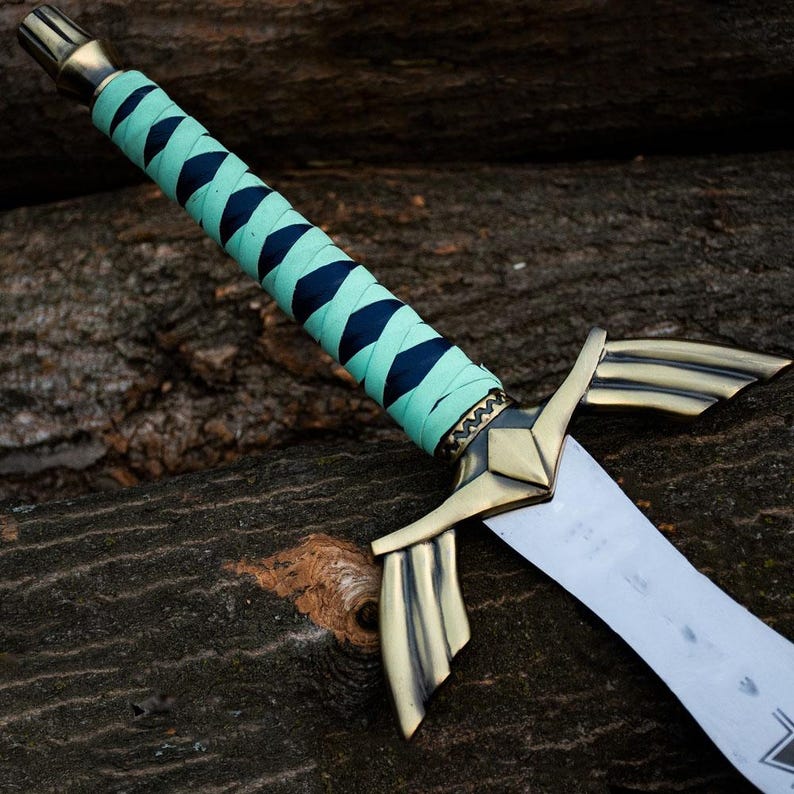 May include: A decorative sword featuring a silver blade and a brass hilt. The handle is wrapped in teal and navy blue fabric. The sword has a stylized crossguard and a detailed pommel. The blade is approximately 30 cm long.