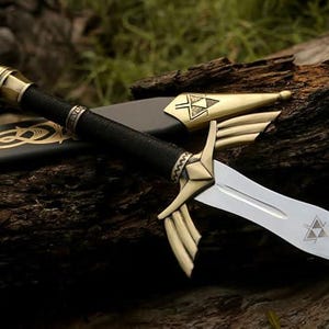 May include: A decorative sword with a silver blade and gold accents. The hilt is black with gold detailing, and the scabbard is black with gold Celtic knotwork. The sword is resting on a piece of wood.