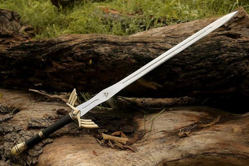 May include: A silver sword with a double-edged blade, featuring a black and gold handle. The sword has a decorative hilt with gold accents and a triangular emblem on the blade. The sword is resting on a weathered log.