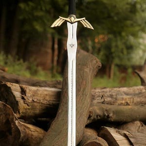 May include: A decorative sword with a silver blade and a black handle. The hilt features gold-coloured wings. The sword is displayed against a backdrop of logs and greenery, suggesting a fantasy or historical theme.
