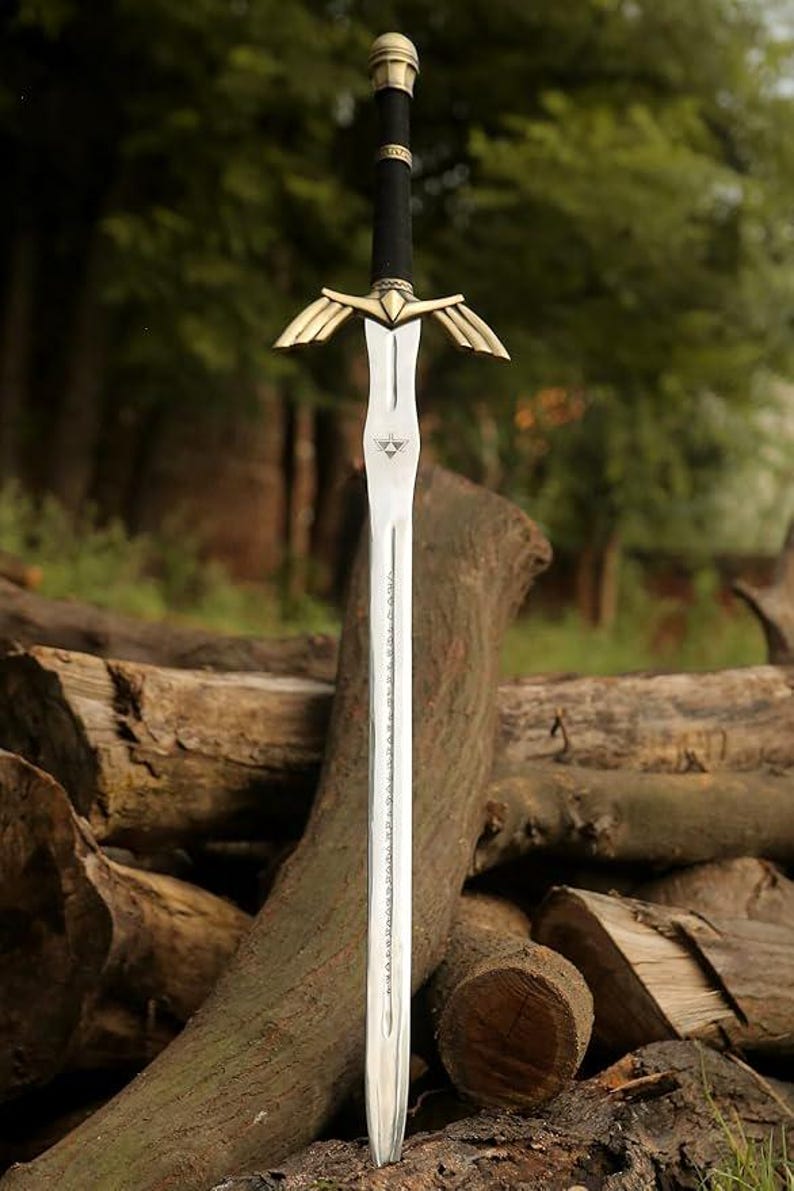 May include: A decorative sword with a silver blade and a black handle. The hilt features gold-coloured wings. The sword is displayed against a backdrop of logs and greenery, suggesting a fantasy or historical theme.