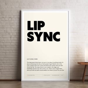 May include: A framed poster with the words "LIP SYNC" in bold black letters on a cream background. The poster is leaning against a white brick wall. A small table and lamp are to the right.