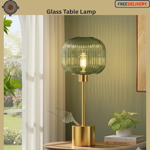May include: A glass table lamp with a ribbed, green lampshade and a gold-colored base. The lamp is turned on by pressing a button on the base. The text "Glass Table Lamp" is at the top of the image.