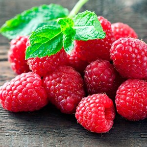 May include: A close-up of a pile of fresh, ripe raspberries. The bright red berries are clustered together, with a few green mint leaves on top. The raspberries are on a dark wooden surface.