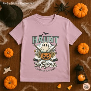 Puede incluir: Camiseta rosa claro con un diseño temático de Halloween. El diseño incluye la palabra "HAUNT" sobre un fantasma, una calabaza tallada y palos de hockey cruzados. También se incluye el texto "The Rink" y "STRONGER TOGETHER". La camiseta está rodeada de calabazas y decoraciones de Halloween.