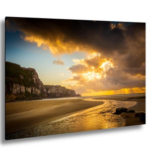 May include: A scenic landscape print featuring a beach with a river flowing into the ocean. The sky is filled with dramatic clouds and golden sunlight. Cliffs are visible on the left side of the image.