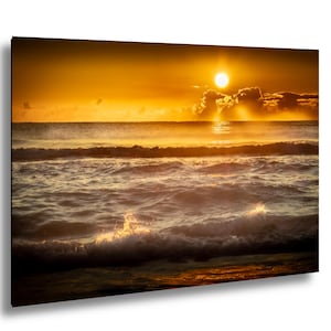 Può includere: Una fotografia vibrante cattura un'alba sull'oceano. Il sole, un globo luminoso, proietta una luce dorata sull'acqua e sul cielo. Le onde si infrangono sulla riva, creando una scena costiera dinamica e serena. La tavolozza dei colori è calda, con sfumature di arancione e giallo.