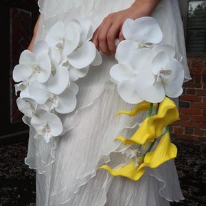 May include: A white wedding dress with a ruffled design. The dress is paired with two bouquets of flowers. One bouquet features white orchids, and the other features yellow calla lilies.
