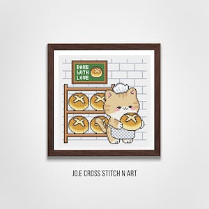 May include: A framed cross stitch pattern featuring a tan cat wearing a white chef hat and apron, holding a round loaf of bread. The background shows a shelf with four loaves of bread and a sign that reads BAKE WITH LOVE. The text JO.E CROSS STITCH N ART is below.