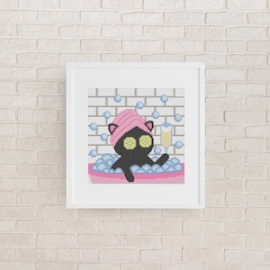 May include: A framed cross-stitch pattern featuring a black cat in a pink bathtub filled with blue bubbles. The cat wears a pink towel wrap on its head and yellow cucumber slices over its eyes, while holding a tall glass of yellow liquid.