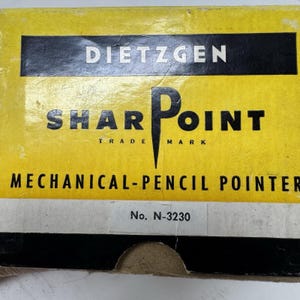 Pode incluir: Uma caixa de produto retangular amarela e preta para um apontador de lápis mecânico Dietzgen Sharpoint. A caixa apresenta texto preto em negrito sobre um fundo amarelo com o número do modelo N-3230 impresso numa etiqueta branca no centro inferior.