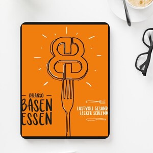 Pode incluir: Um tablet laranja com o texto "BALANSO BASEN ESSEN" e "LUSTVOLL GESUND LECKER SCHLEMM" em preto. Um grande número oito é desenhado acima de um garfo. Uma xícara de café e óculos estão no fundo.