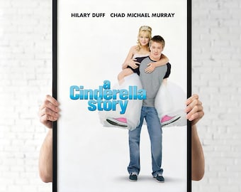 May include: A framed movie poster for "A Cinderella Story" featuring Hilary Duff and Chad Michael Murray. The poster has a black frame and shows the actors in a romantic pose, with the movie title in blue. The background is white.