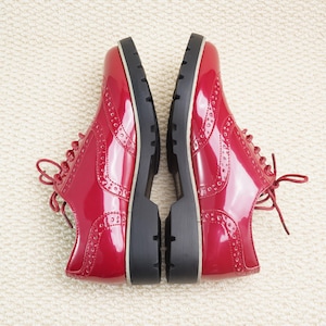 Peut inclure: Paire de chaussures oxford rouges brillantes avec des perforations d&eacute;coratives et des semelles noires &eacute;paisses. Les chaussures sont lac&eacute;es et c&ocirc;te &agrave; c&ocirc;te, mettant en valeur leur design. Un choix de chaussures &eacute;l&eacute;gant.