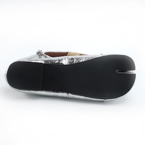 May include: Silver ballet flats with a split-toe design. The shoes have a metallic finish and a black rubber sole. The flats are a unique style of footwear.