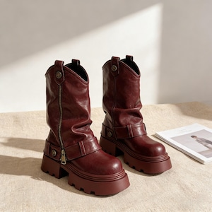 Peut inclure: Bottes de cheville bordeaux d'inspiration western. Elles présentent une fermeture éclair, des boucles et une semelle plateforme épaisse. Les bottes sont en matière simili cuir. Hauteur d'environ 15 cm.