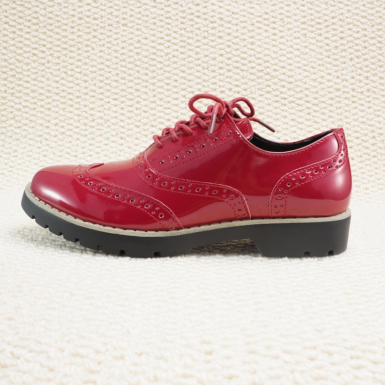 Peut inclure: Une paire de chaussures Oxford en cuir verni rouge avec un design brogue classique. Les chaussures ont une finition brillante, une semelle noire et des lacets rouges. Les chaussures mesurent environ 25 cm de long.
