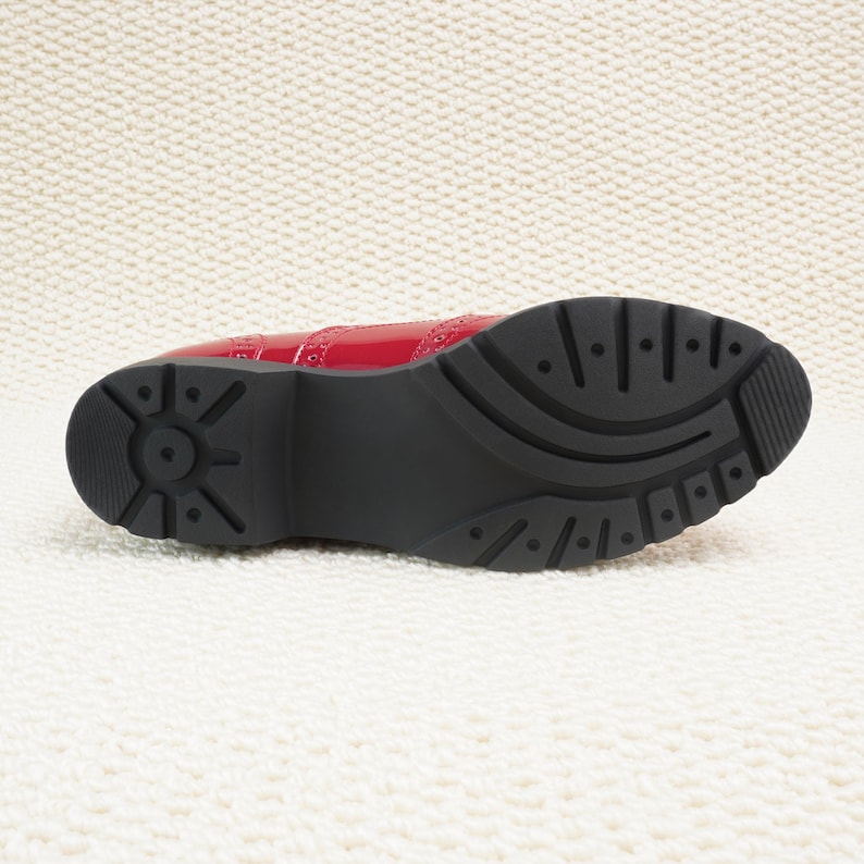 Peut inclure: Une chaussure en cuir verni rouge avec une semelle en caoutchouc noire. La chaussure pr&eacute;sente un design brogue classique avec des perforations d&eacute;coratives. La semelle a un motif textur&eacute; pour l'adh&eacute;rence.
