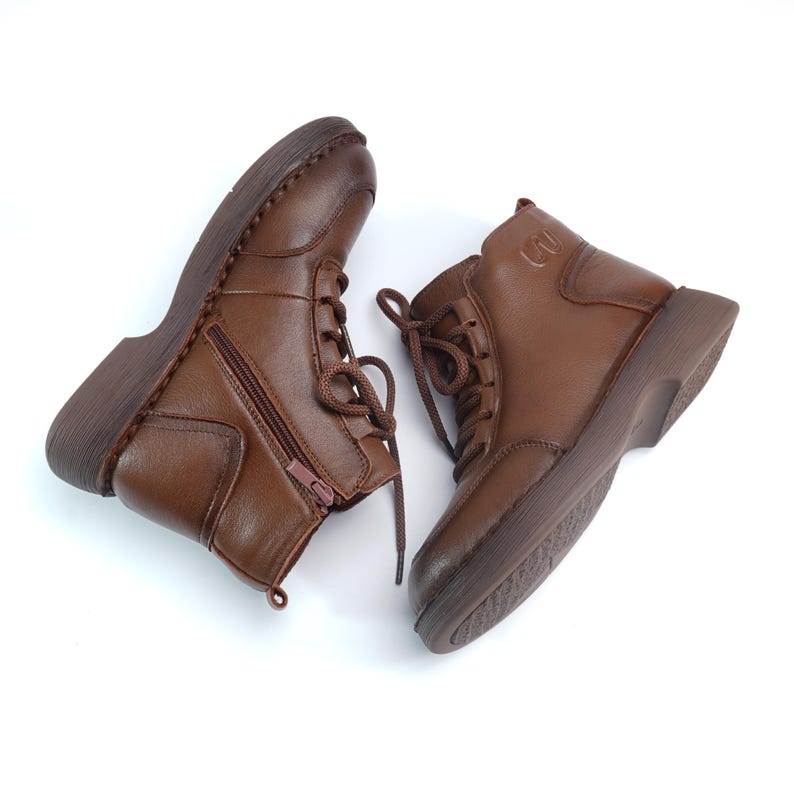 Puede incluir: Botines de cuero marr&oacute;n con cordones y cremalleras laterales. Las botas tienen punta redonda y suela gruesa. El cuero parece liso, sobre fondo blanco. Adecuadas para diversas ocasiones.