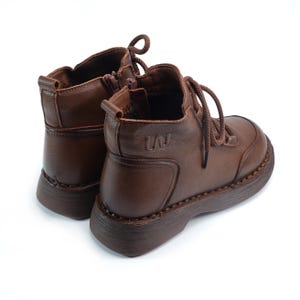 Puede incluir: Botines de cuero marr&oacute;n con punta redondeada y suela gruesa. Las botas tienen cierre de cordones y cremallera lateral. Las botas tienen un peque&ntilde;o dise&ntilde;o en relieve en el lateral. Sobre fondo blanco.