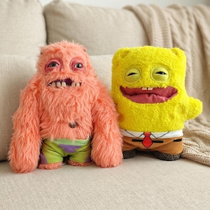 May include: Two plush toys: a pink, furry creature wearing green and purple shorts, and a yellow, square-shaped character with a red tie and brown trousers. Both have exaggerated facial features and are on a beige sofa.