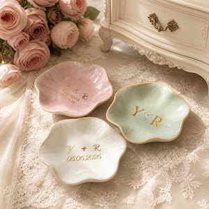 May include: Three flower-shaped ceramic trinket dishes in pastel pink, mint green, and white. Each dish features gold-colored lettering: the pink dish reads Y & R Engaged 04.24.26, the green dish reads Y heart R, and the white dish reads Y + R 06.06.2026.