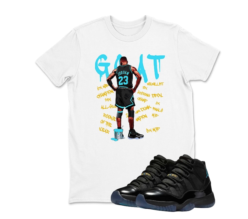 May include: White t-shirt featuring a basketball player graphic and the word "GOAT" in turquoise. Black and turquoise basketball trainers are in the foreground. The shirt design includes the number 23 and other text.