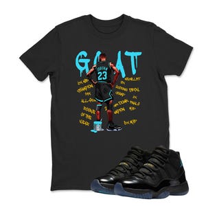 May include: Black t-shirt with turquoise graffiti-style lettering spelling "GOAT". A graphic of a basketball player is on the shirt, along with text. Black and turquoise basketball trainers are in the foreground.
