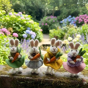 May include: Four handmade felt bunny figurines, each holding a carrot. The bunnies wear different colored outfits: green, gray, yellow, and pink. They stand on a mossy surface with a lush garden background filled with colorful flowers.