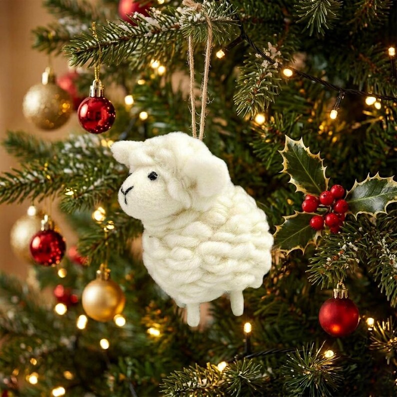 May include: A white needle-felted sheep ornament with a textured, woolly body and a simple stitched face. The sheep is suspended by a thin brown twine loop, designed to hang from a branch as a decorative holiday tree ornament.