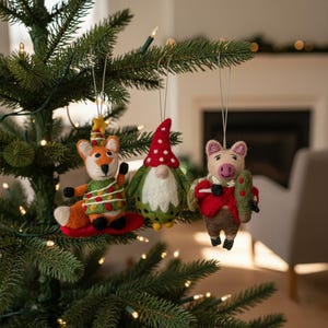 Peut inclure: Trois décorations de Noël faites à la main : un renard avec un chapeau, un gnome avec un chapeau rouge à pois et un cochon tenant un arbre. Les ornements sont en feutre et ont des attaches. Accrochés à un sapin de Noël vert.