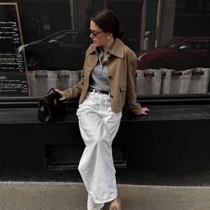 Model wearing beige leather jacket styled with white trousers and classic minimalist outfit