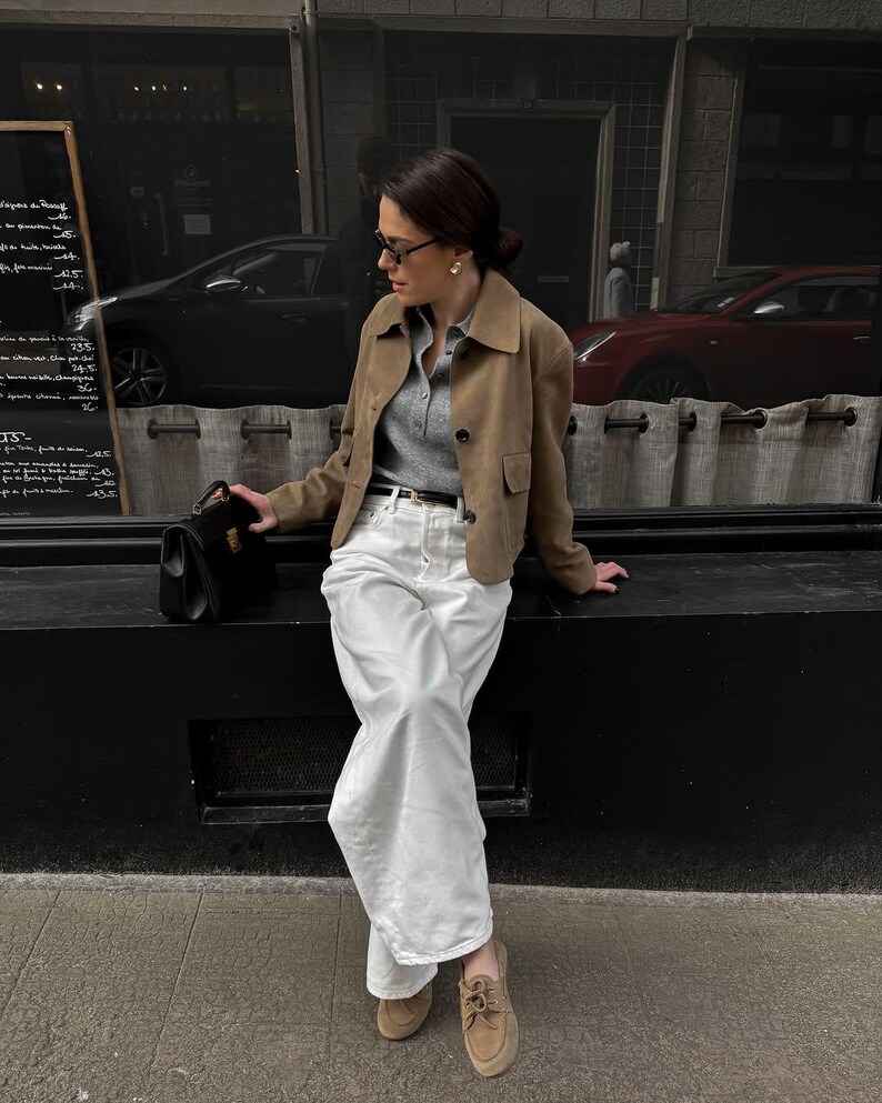 Model wearing beige leather jacket styled with white trousers and classic minimalist outfit