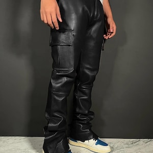 Puede incluir: Pantalones cargo de cuero negro con diseño de pernera recta. Los pantalones tienen un bolsillo en cada muslo y se combinan con zapatillas deportivas azules y blancas. Los pantalones están hechos de un material brillante y liso.