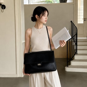 May include: A black leather shoulder bag with a rectangular flap, a silver-toned metal turn-lock closure, and a thin shoulder strap. The bag features a textured surface and a structured silhouette, providing a clean and functional design for daily use.
